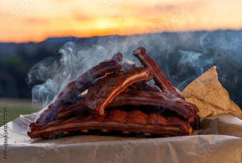 Juicy smoked ribs stacked on parchment, with wisps of smoke rising against a warm sunset. Ideal for barbecue, outdoor cooking, family meals, and flavorful meat dishes.