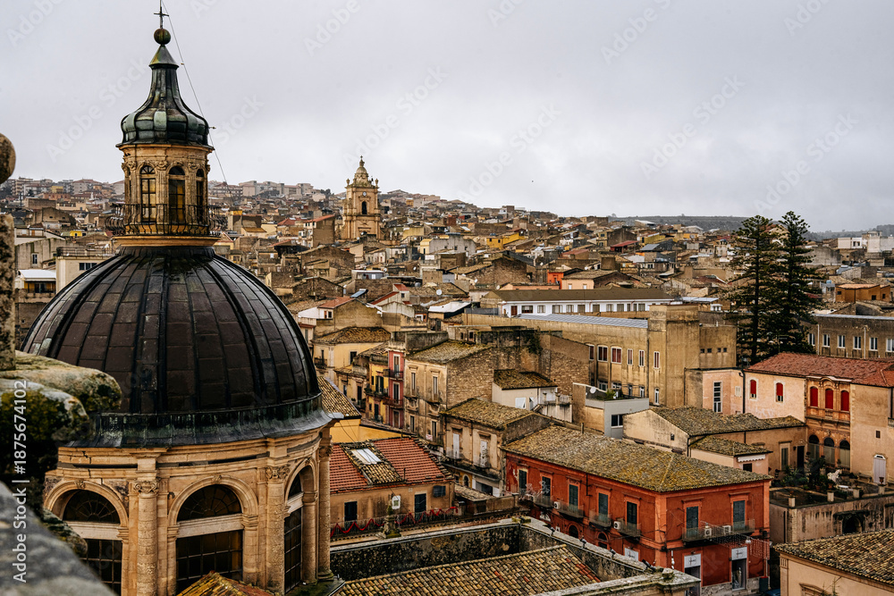 Fototapeta premium Panoramic View Over Ragusa From Cathedral Of San Giovanni Battista: Historic Sicilian City Rooftops, Church Domes, And Dense Stone Architecture Under Overcast Sky