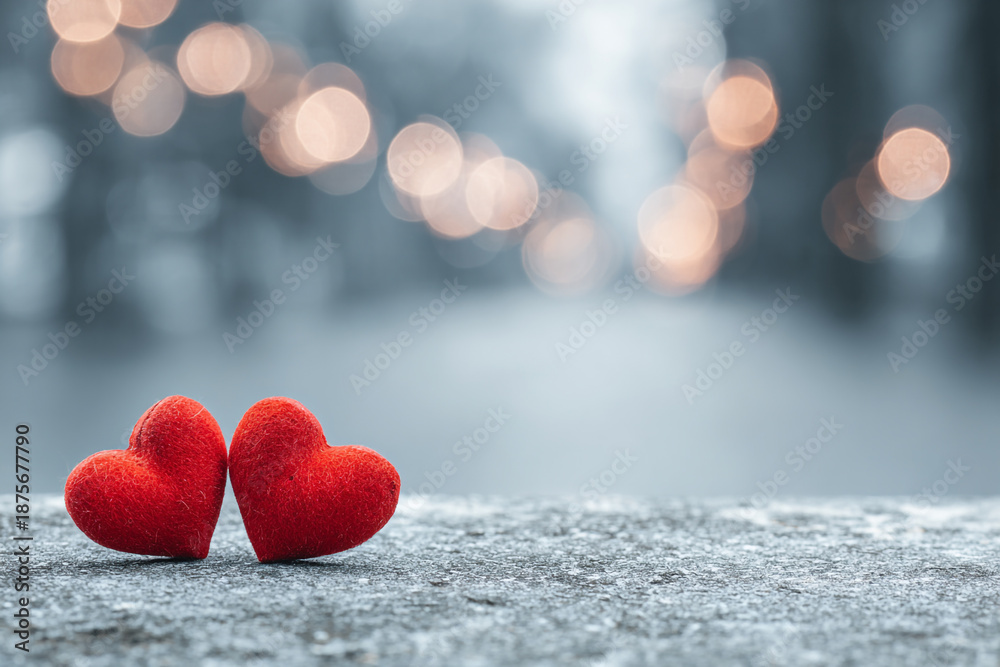 Fototapeta premium two fluffy red hearts sit on a textured grey surface with a soft focus background of glowing lights