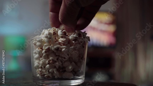 Popcorn in a cup in front of the TV. A hand takes popcorn from a cup.