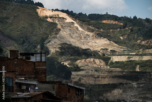 View of a dramatic mountainside scarred by quarrying behind a cluster of modest brick homes, a stark contrast of nature and industry, Medellin, Colombia.