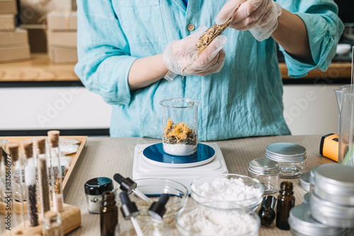 Canvas-taulu Person in protective gloves pours dried herbs from plastic bag into glass beaker on digital scale