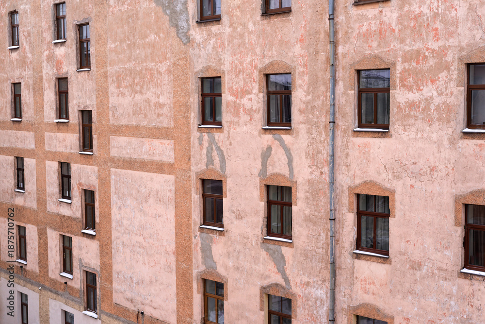 Obraz premium Vintage apartment building facade with repetitive windows and cracked plaster texture