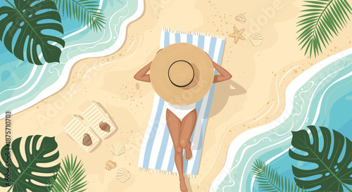 Overhead view of a woman in a large sun hat relaxing on a beach towel between ocean waves and tropical palm leaves.