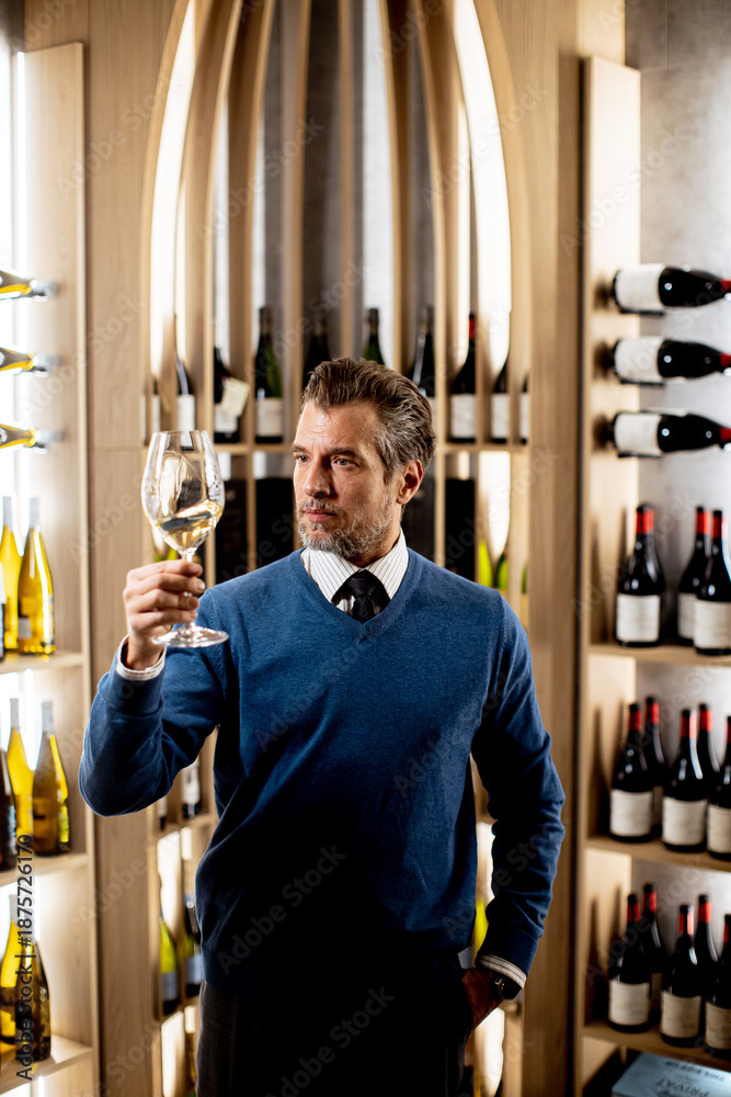 Fototapeta premium Man enjoying fine wine in a stylish modern wine cellar while examining glass