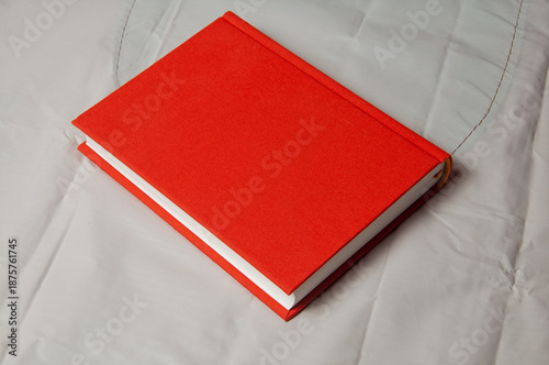 Fotografie A closed red hardcover book rests on a textured white surface
