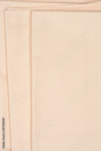 A top view of stacked layers of light beige cotton fabric with a subtle dotted pattern and clean edges providing a neutral textile background