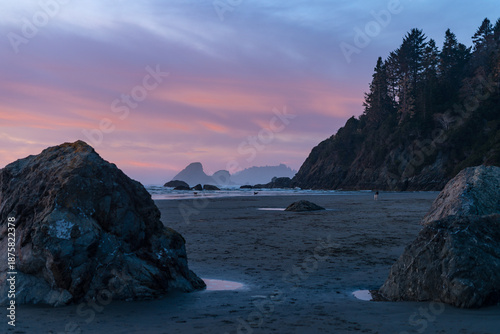 Tranquil sunrise at Moonstone Beach in Trinidad, California. Receding tide creates reflective ripples on dark sand with Camel Rock and sea stacks silhouetted against a vibrant orange and pink sky.