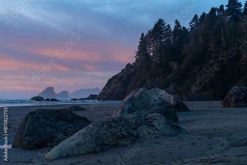 Tranquil sunrise at Moonstone Beach in Trinidad, California. Receding tide creates reflective ripples on dark sand with Camel Rock and sea stacks silhouetted against a vibrant orange and pink sky.