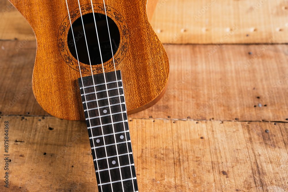 Obraz premium A classic brown acoustic ukulele with white wooden strings rests on a rustic wooden table like a folk musical instrument ready to play a jazz and rock music concert