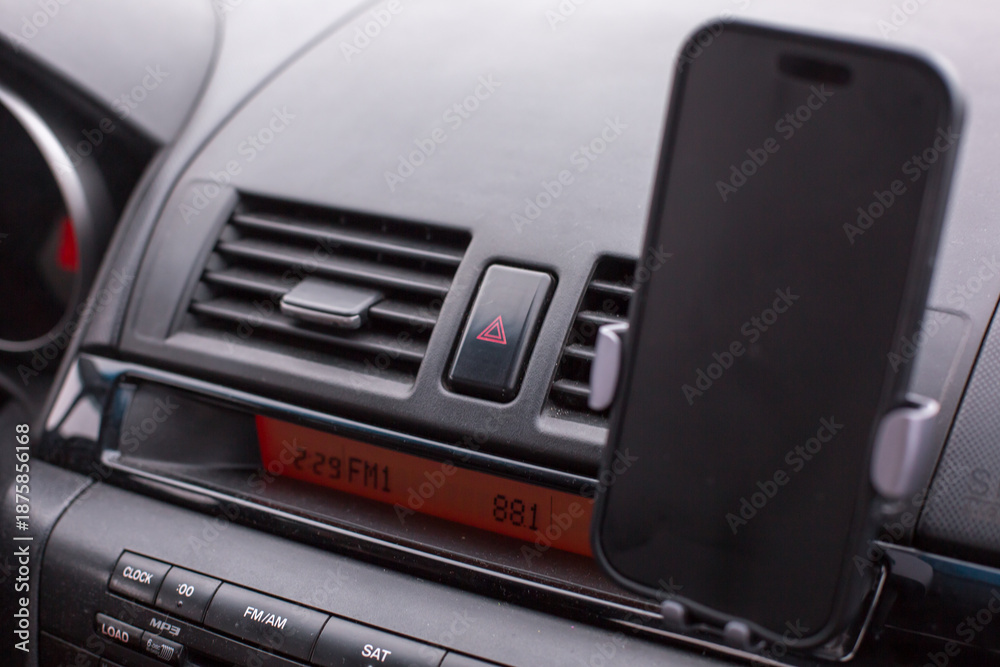 Fototapeta premium Smartphone mounted in car dashboard holder, displaying radio frequency, with air vents and control panel visible, illustrating modern vehicle technology and convenience