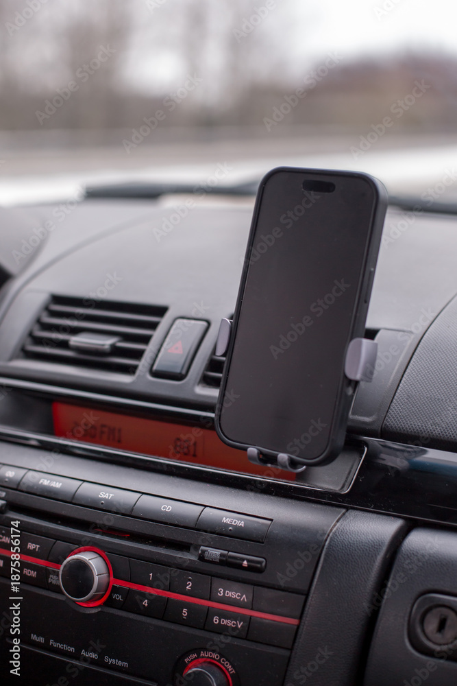 Fototapeta premium Smartphone mounted in a car dashboard holder, showcasing a sleek design and modern technology, with a blurred road view in the background, emphasizing convenience and safety