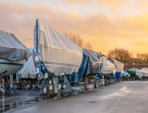 Photos Row of boats wrapped and stored outdoors at boatyard.