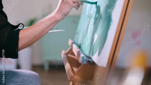 The artist paints a picture. A woman applies paint to a canvas with a brush in the studio. Close-up of hand.