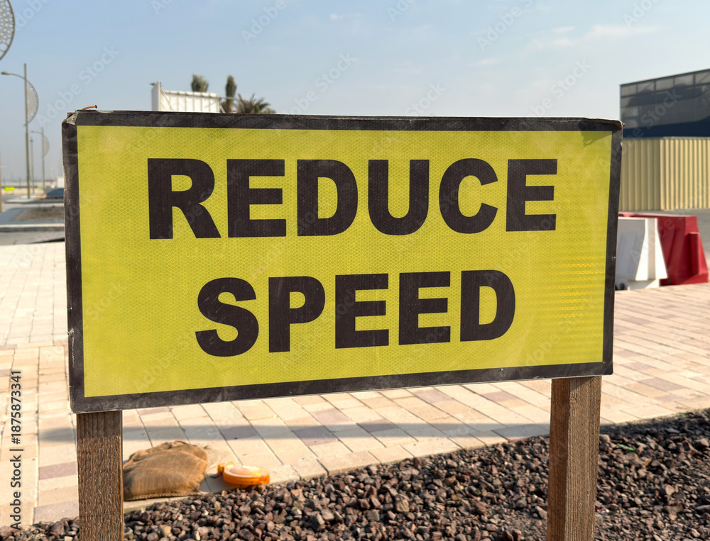Fototapeta premium Urban road sign with bold Reduce Speed warning for traffic safety in modern city infrastructure.