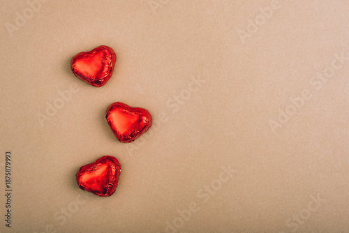 Three red foil wrapped chocolate hearts on brown paper background with copy space