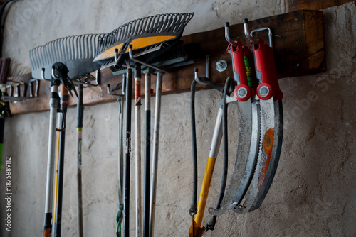 Fotografija Wall mounted rack holding rakes, long handle yard tools and red handled sickle s