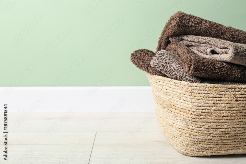 Obraz premium Laundry basket with towels on floor near green wall indoors, closeup. Space for text