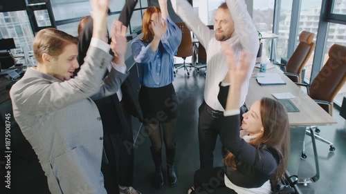 A group of professionals work together in a modern office setting, showing teamwork and support. One team member in a wheelchair joins the circle of hands.