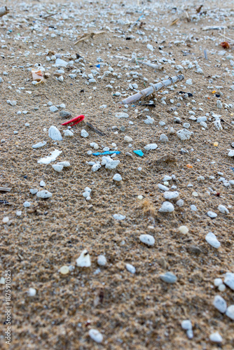 Sandy beach contaminated with micro-plastics. Close-up view of microplastics and trash on a beach. 