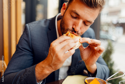Quadro em tela Businessman in a suit eating a delicious sandwich, hungry male professional having a quick lunch break during work