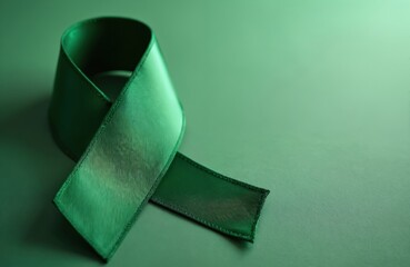 Green awareness ribbon lies on matching green backdrop. Symbolizes support for disease awareness campaigns, health charities, and mental health advocacy. Offers copy space for text.