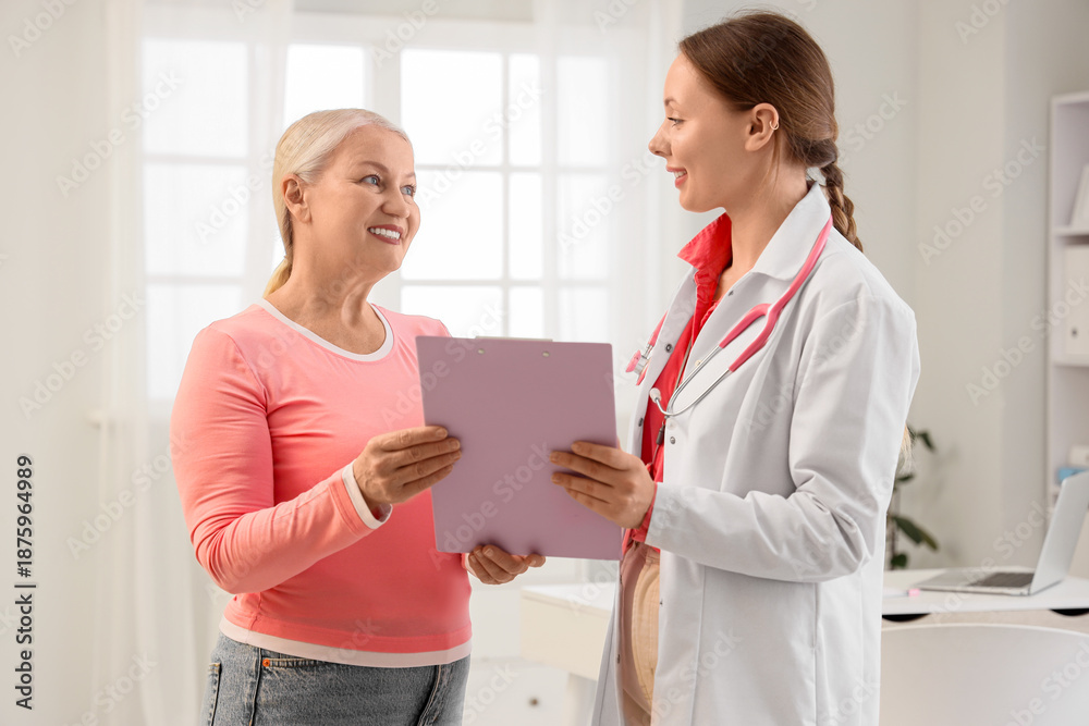 Obraz premium Mature woman and gynecologist with clipboard in clinic. Menopause concept
