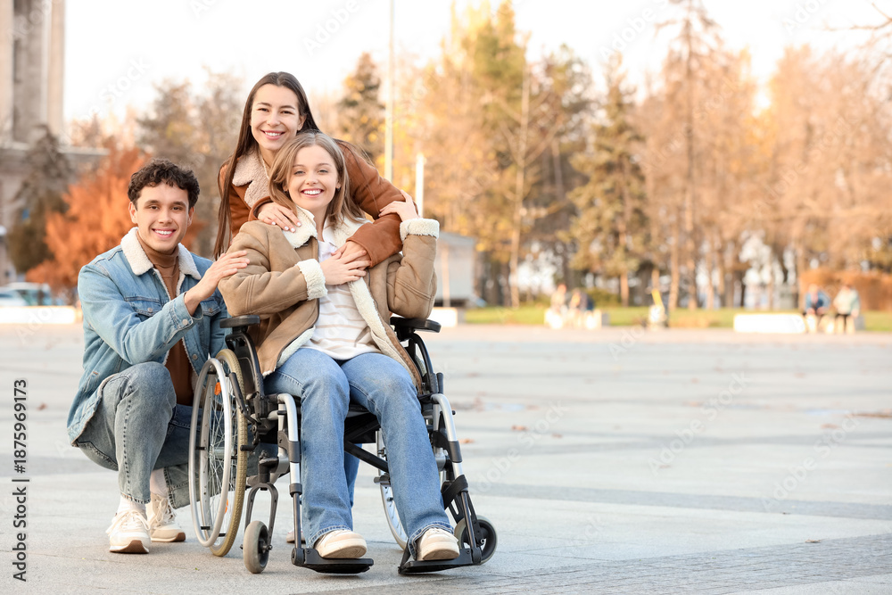 Fototapeta premium Young woman in wheelchair with her friends hugging on city square
