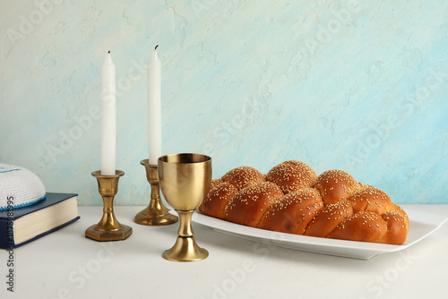Traditional challah bread with goblet for wine and burning candles on white table. Shabbat Shalom
