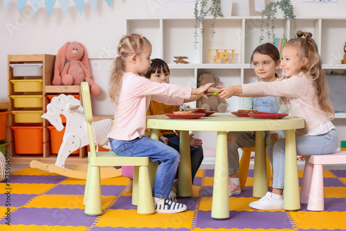 Group of little children having lunch at table in kindergarten