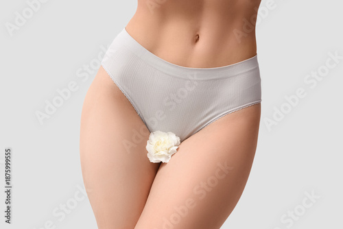 Tableau sur toile Young woman in panties with flower on light background, closeup