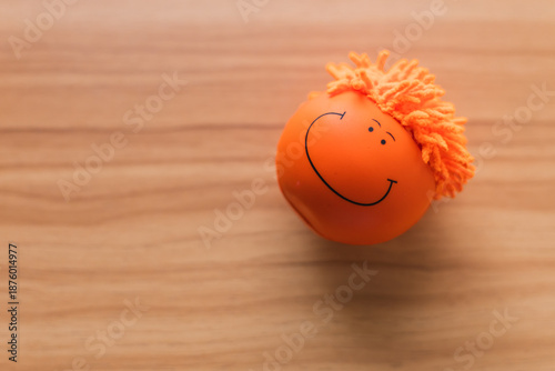 PELOTA DESESTRESANTE DE COLOR NARANJA CON UNA CARA FELIZ SOBRE UNA MESA