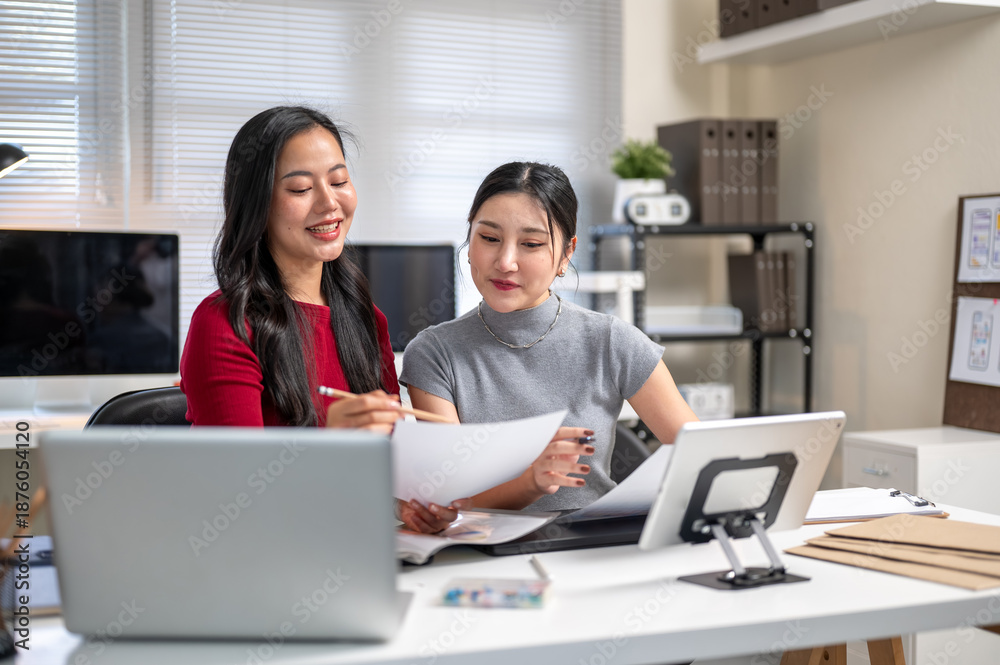 Obraz premium Pretty asian woman and coworker looking at working material document together on table in the office