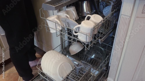 Adult woman arranging plates and cups inside open dishwasher at home. Domestic work, cleanliness and daily routine concept.