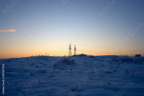 winter morning landscape of snow covered nature, trees and large poles of high voltage power transmission lines
