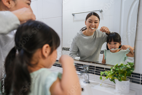 Принти на полотні mother teaching girl child to brushing teeth at reflection in mirror in bathroom