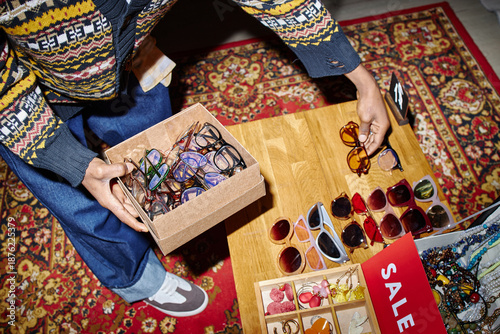 Tableau sur toile Young adult Black man sorting second hand sunglasses on wooden table, holding ca