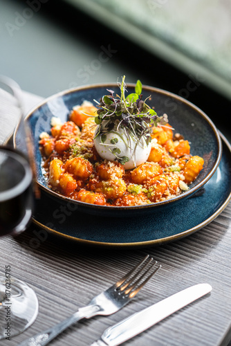 Photos A gourmet plate of handmade potato gnocchi tossed in a rich tomato basil sauce, topped with a fresh creamy burrata ball, grated parmesan cheese, and delicate microgreens in a dark restaurant setting