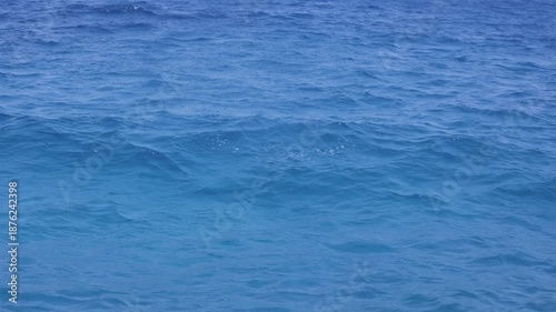 Close-up view of blue ocean water with gentle waves and a small splash in the center. Slow motion.