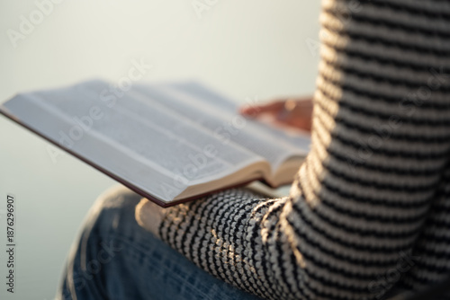 The image depicts a woman reading the Bible outdoors in soft sunlight. The concept encompasses reading the Bible and seeking God's words in the sacred texts, spiritual growth, and daily devotion.