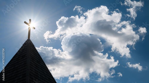 Silhouette of a church steeple with a cross against a bright blue sky. Sun shining through the cross with drifting clouds. Christianity and faith concept. Copy space for text