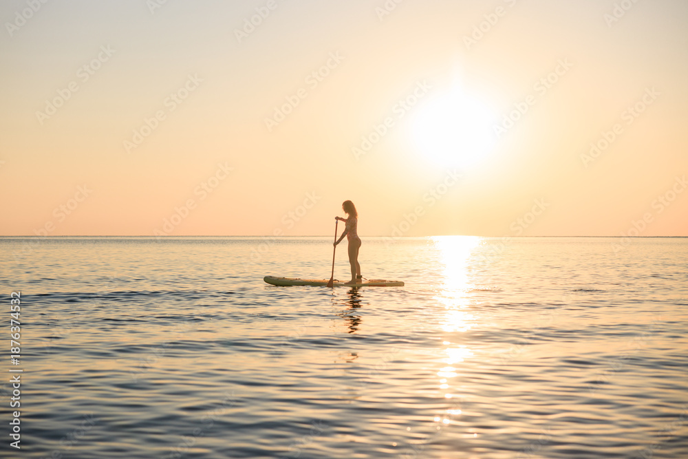 Fototapeta premium Young woman walking on stand up paddle sup boards by the sea during summer vacation