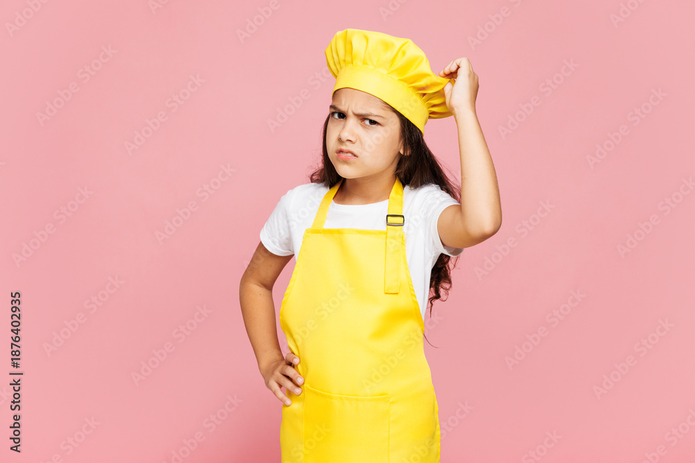 © ViDi Studio - Small confused puzzled minded kid child girl housewife chef cook baker mother's helper wear yellow apron toque cap scratch head temple isolated on pastel plain pink background. Cooking food concept.