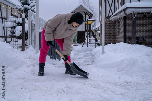 Картината върху платно Woman shoveling snow from driveway after heavy snowfall near private house