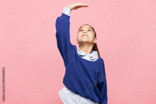 Quadro em tela Little child kid girl 8-9 years old wears blue shirt have fun hold hand above head show how much she grown, try to be taller isolated on pink background