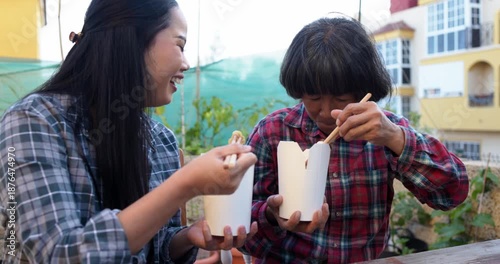 Asian mother and daughter having fun during lunch time eating together instant noodles at home terrace - Family lifestyle and food concept 