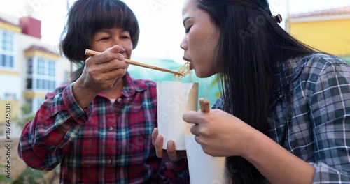 Asian mother and daughter having fun eating together instant noodles outdoor at home terrace - Family lifestyle and food concept 