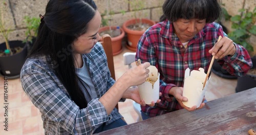 Asian mother and daughter eating together instant noodles outdoor at home terrace - Family lifestyle and food concept 