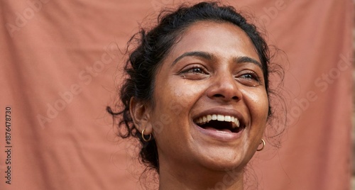 South Asian woman laughing with tears in her eyes against a brown background


