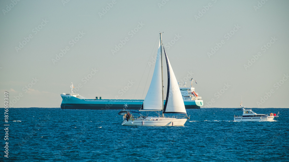 Fototapeta premium Sailboat, Motorboat, and Cargo Ship on Open Sea